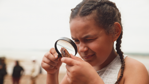 Young child examines a rock with a magnifying glass. 