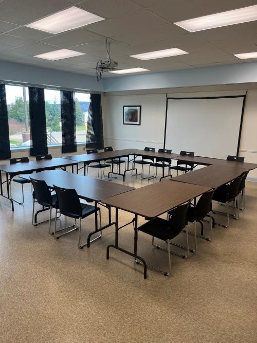 Bright, open concept room with tables, chairs, and projector screen set up. 