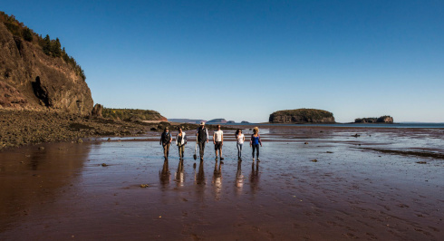 Six people in the distance walking on a beach on the Bay of Fundy.