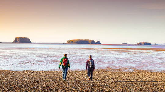 Two people wearing backpacks on the beach looking our at Five Island Provincial Park 